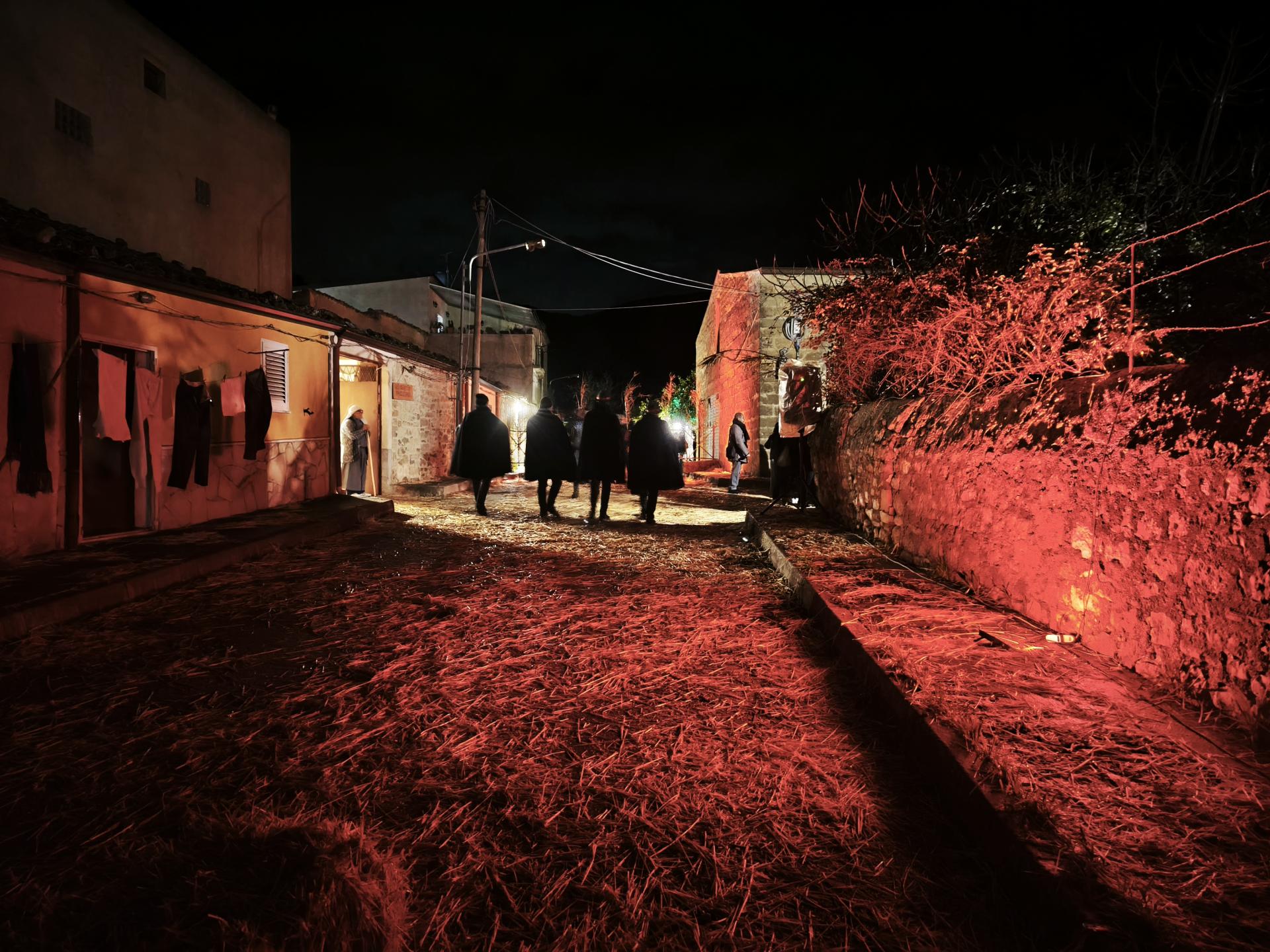Scorcio del Presepe Vivente di San Carlo con figuranti in costume d’epoca, botteghe artigiane illuminate e scene della Natività lungo le vie del borgo durante il periodo natalizio.